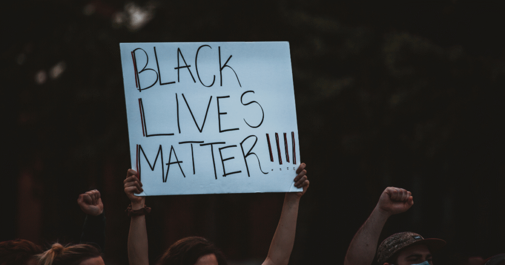 imagem de protesto de antirracismo com uma mulher segurando uma imagem onde se lê black lives matter
